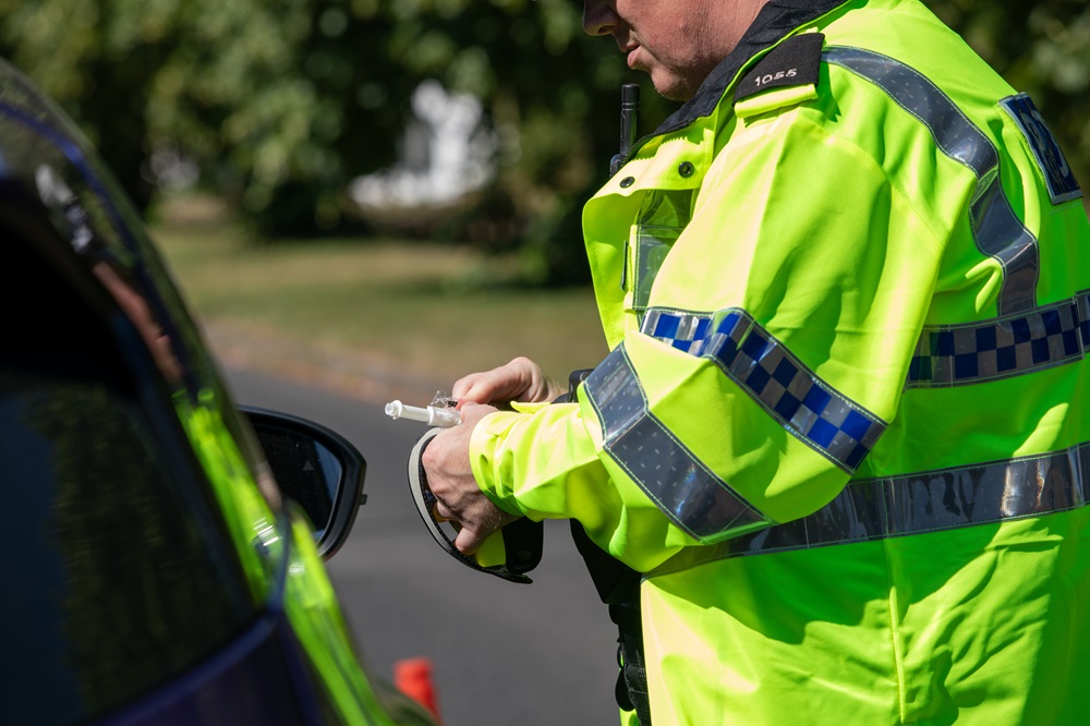 A POLICE OFFICER TAKES A BREATH TEST BY THE ROAD SIDE